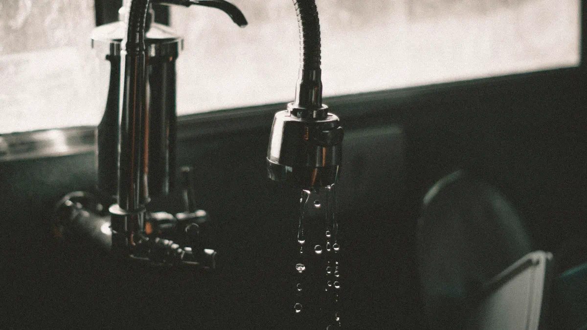 Water droplets falling from a dark kitchen faucet