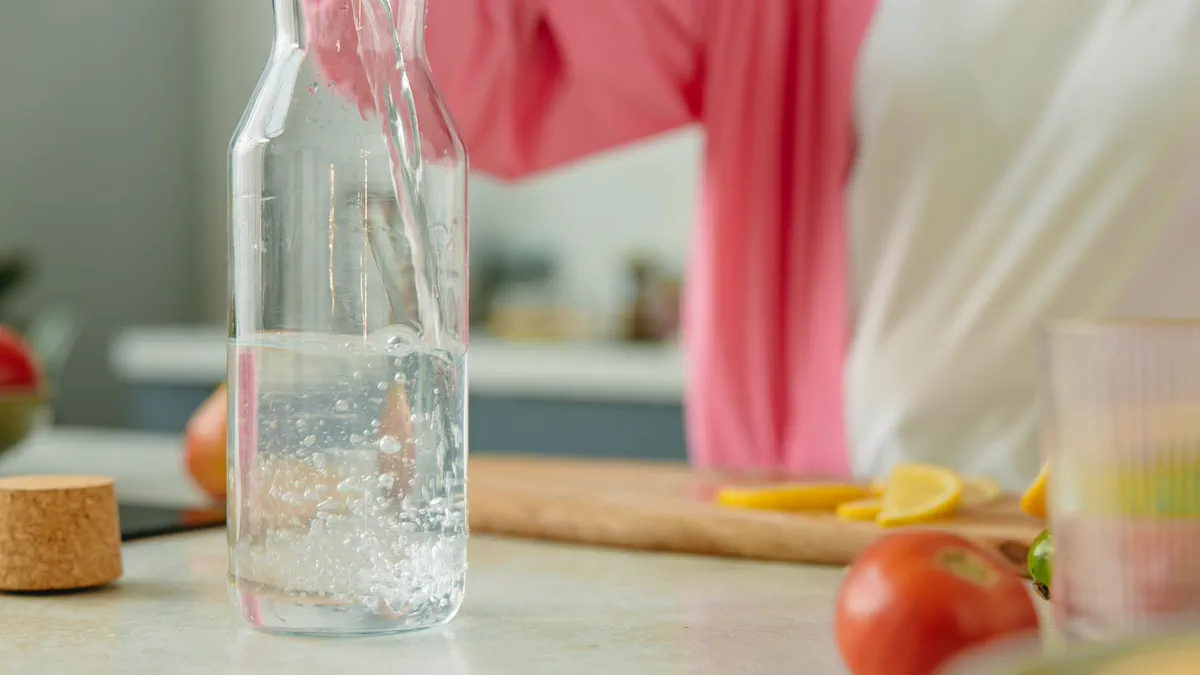 Clear water being poured into a glass bottle on a kitchen counter